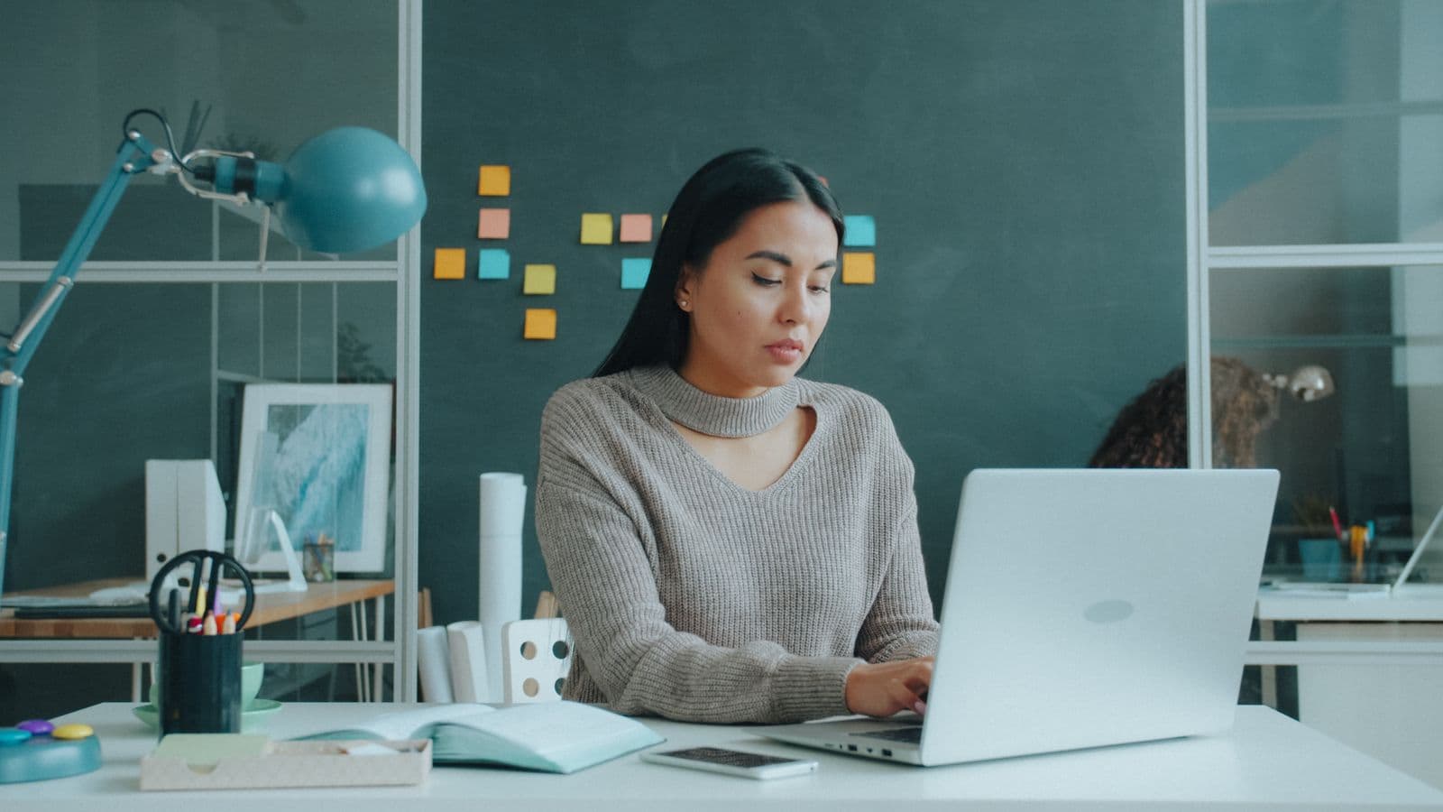 A woman working at a laptop at a desk with notes on the wall