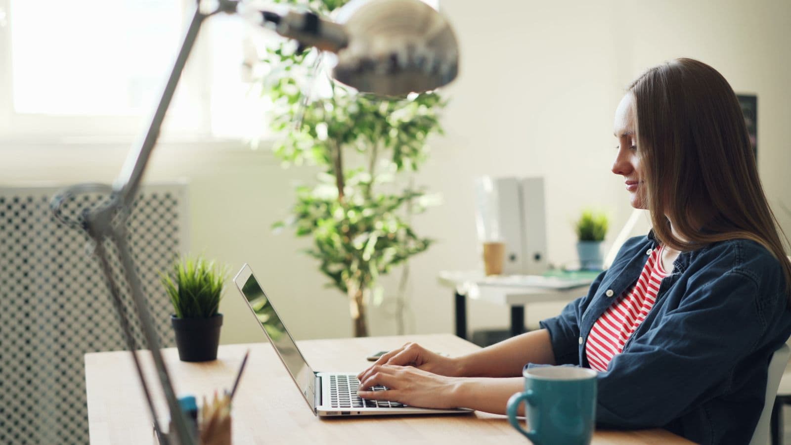 A woman working on a laptop in a bright office with plants